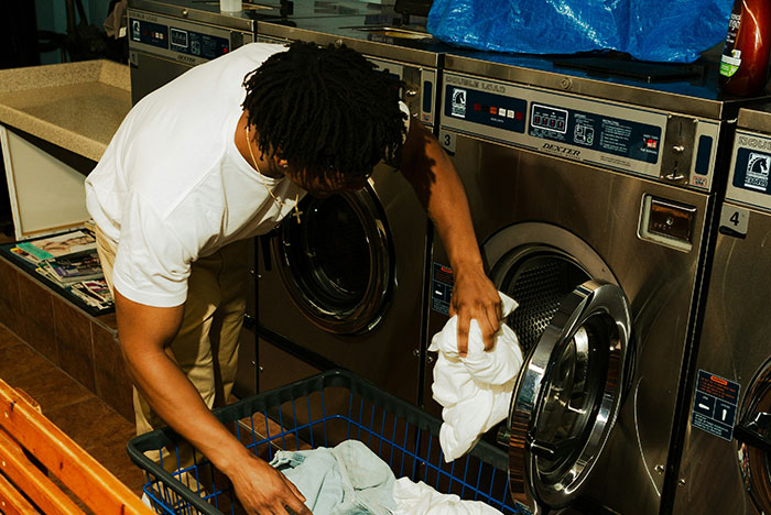 Person loading laundry into a washing machine at a laundromat, illustrating instant karma moments with everyday tasks.