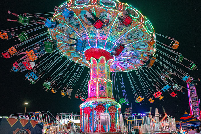 Colorful illuminated swing ride at night, capturing a moment of instant karma as a chair flips unexpectedly mid-ride.