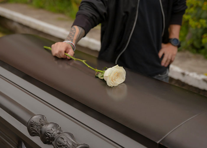 Person placing a white rose on a dark coffin, symbolizing a poignant moment linked to Rihanna Slapped Him facts.