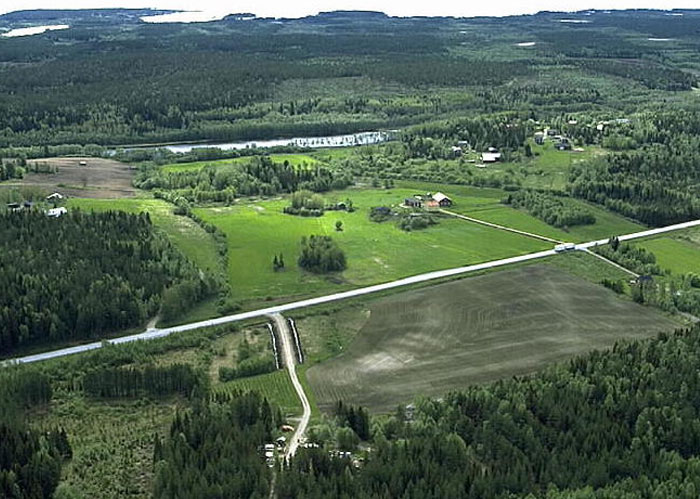 Aerial view of rural landscape with green fields, forests, and scattered houses under a cloudy sky.