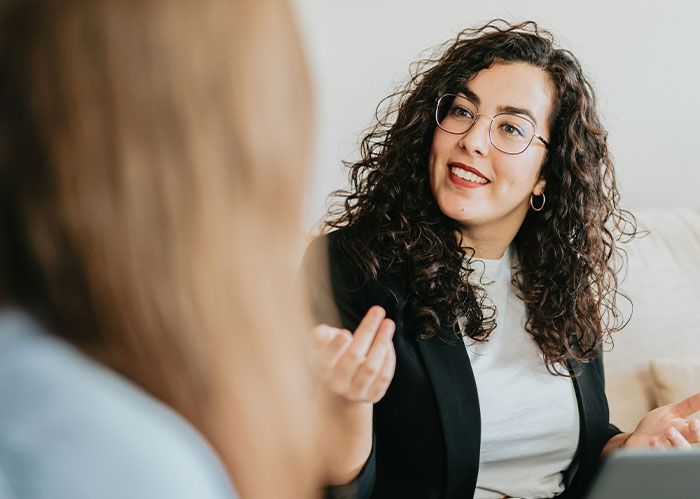 Woman with curly hair and glasses explaining Rihanna slapped him story during a casual conversation indoors.