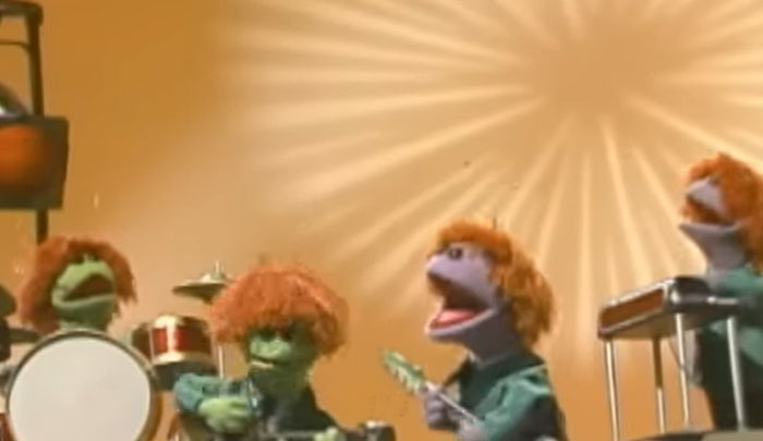 Green puppets with orange hair playing instruments in a band, referencing Rihanna slapped him in a playful scene.