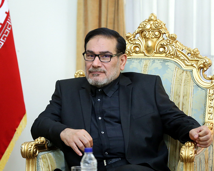 Iranian politician seated on an ornate chair with a red flag in the background amid risqu&eacute; wedding dress outrage.