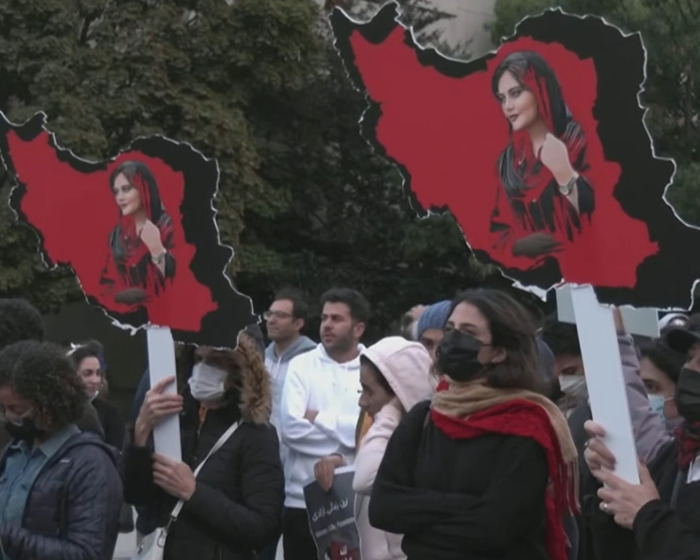 Protesters holding signs showing risqu&eacute; wedding dress of Iranian politician's daughter amid headscarf surveillance debate.