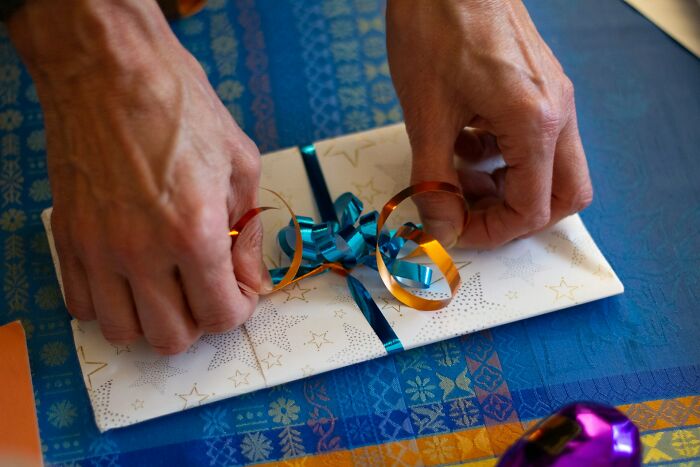 Hands tying blue and orange ribbon on a star-patterned gift wrapping, symbolizing wedding guests causing regret for bride and groom.