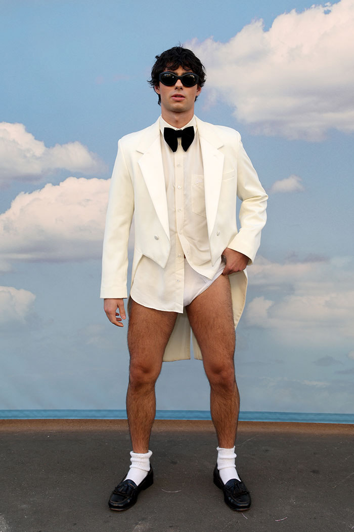Man wearing a white tuxedo jacket with bow tie, underwear, black shoes, and sunglasses showcasing weird celebrity looks Vogue World 2025.