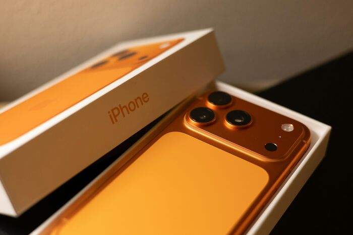 Orange iPhone in an open box, highlighting technology skills challenges parents often face in a funny way.