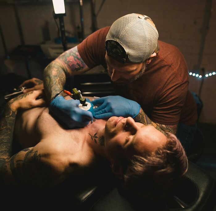 Tattoo artist working on a client's chest tattoo with precision and focus in a dimly lit studio environment.