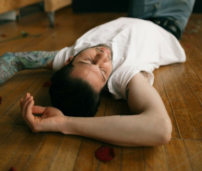 Man with tattooed arm lying on wooden floor, appearing distressed, illustrating tattoo artists messed up moments.