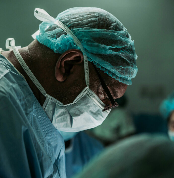 Surgeon focused during operation, wearing surgical mask and cap, showcasing protection and care for people's safety.