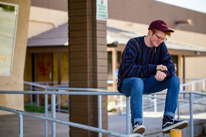 Teen boy sitting alone outside school wearing a cap and striped sweater, reflecting on popular kids turning into outcasts.