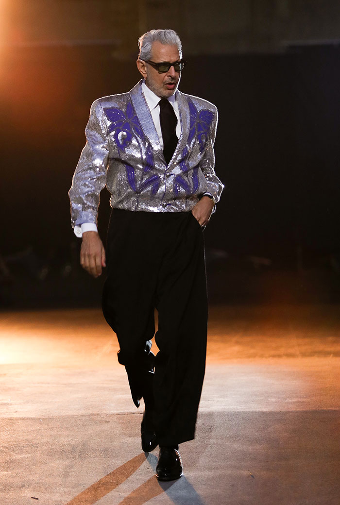 Man in oversized silver jacket with purple design, black pants, and sunglasses showcasing weird celebrity looks Vogue World 2025.