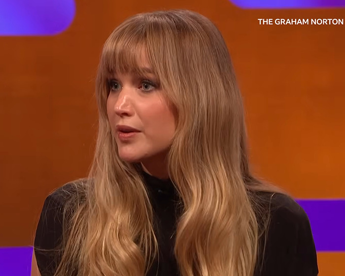 Jennifer Lawrence with long blonde hair and black top giving a heated response during a television interview on Graham Norton.