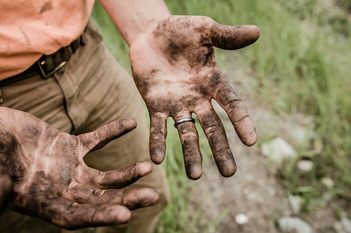 Close-up of dirty hands covered in soil, representing hard work and common truths behind propaganda beliefs.