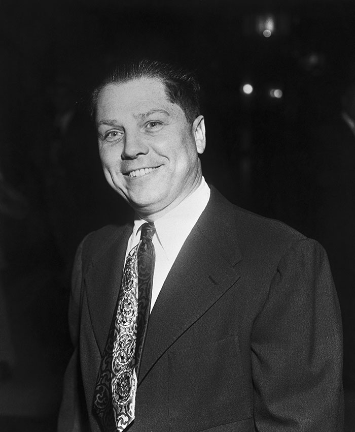 Figura pública sonriendo con traje y corbata en evento nocturno, relacionado con figuras desaparecidas sin dejar rastro.