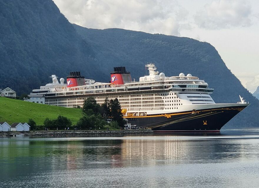 Disney cruise ship docked near green hills and calm waters, highlighting mom's behavior in terrifying girl's ocean plunge incident.