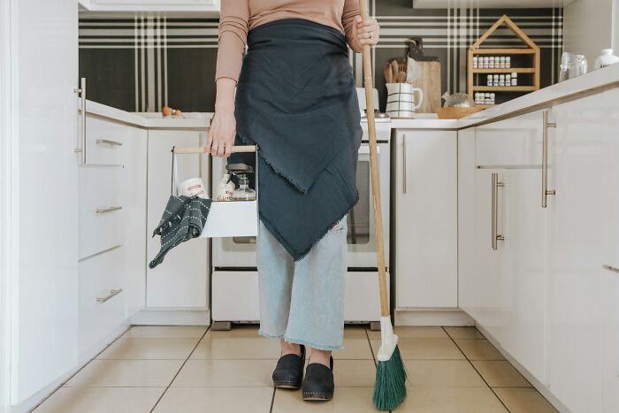 Person in a modern kitchen holding cleaning supplies and a broom, representing practical relationship advice for couples.