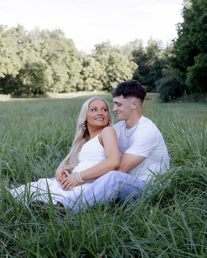 Young couple sitting in a grassy field, relating to the Laken Snelling baby case as new evidence sparks public fury.
