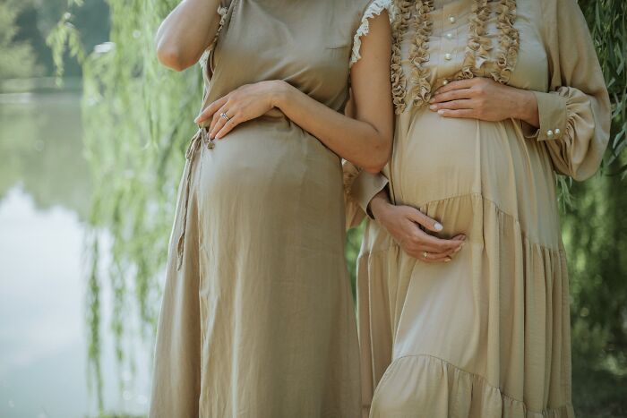 Two pregnant women standing outdoors, gently holding their baby bumps in a serene, natural setting.