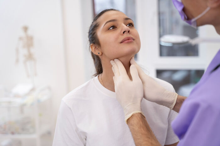 Doctor examining young woman's neck in clinic, highlighting times people were told they were just anxious health issues.