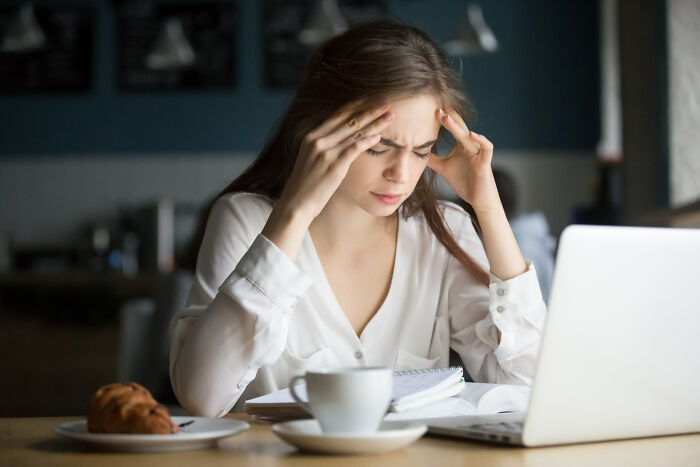 Young woman at a laptop holding her head in stress, representing people told they were just anxious facing real issues.