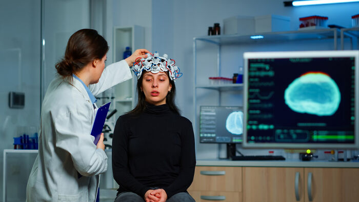 Doctor placing EEG cap on anxious woman’s head during brain activity test in clinical setting for anxiety diagnosis.
