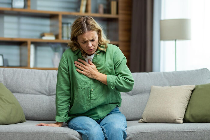 Woman sitting on a couch clutching her chest in discomfort, illustrating symptoms often mistaken for anxiety issues.
