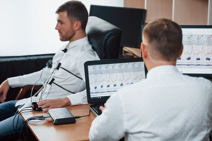 Man undergoing a polygraph test monitored by a technician analyzing anxiety-related physiological responses on screens.