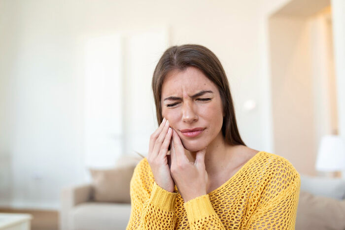 Young woman in a yellow sweater touching her cheek, showing discomfort linked to anxiety symptoms and serious health concerns.
