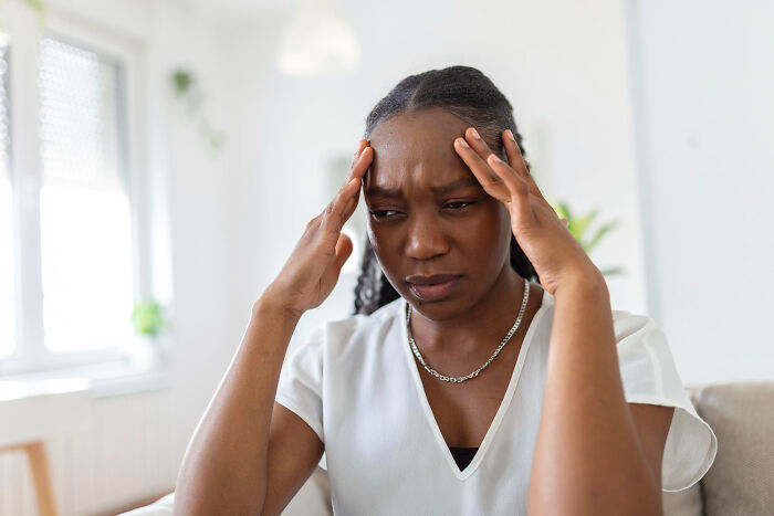 Woman experiencing stress and anxiety, holding her head with hands in a bright, calm indoor space