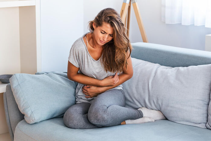 Young woman clutching her stomach in pain on a couch, illustrating hidden issues often mistaken for anxiety symptoms.