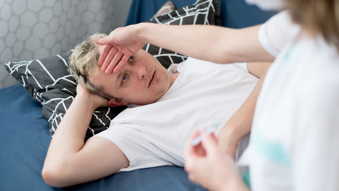 Young man lying in bed looking anxious while talking to a healthcare professional about actual health issues beyond anxiety.