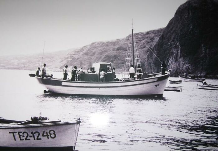 Black and white photo of people on a fishing boat in the ocean near rocky cliffs capturing weird and fascinating ocean moments.