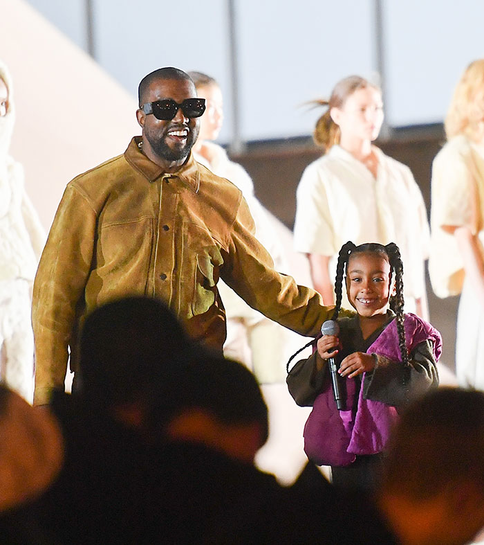 Kanye West standing with daughter North West holding a microphone during a public event amid online life concerns.