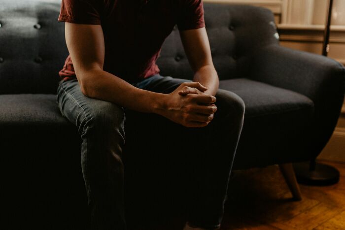 Man sitting on dark couch with hands clasped, representing dark secrets that could ruin people’s lives if revealed.
