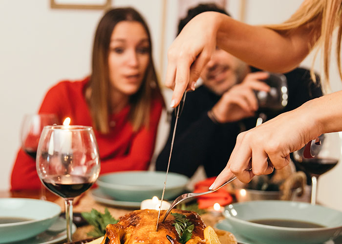 Woman carving Thanksgiving dinner turkey with family seated, highlighting tension around conservative uncle during holiday meal.