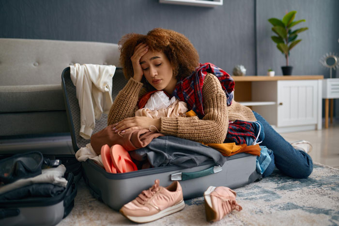 Young woman overwhelmed with packing clothes in suitcase, representing homeless friend mooching off couple for months.