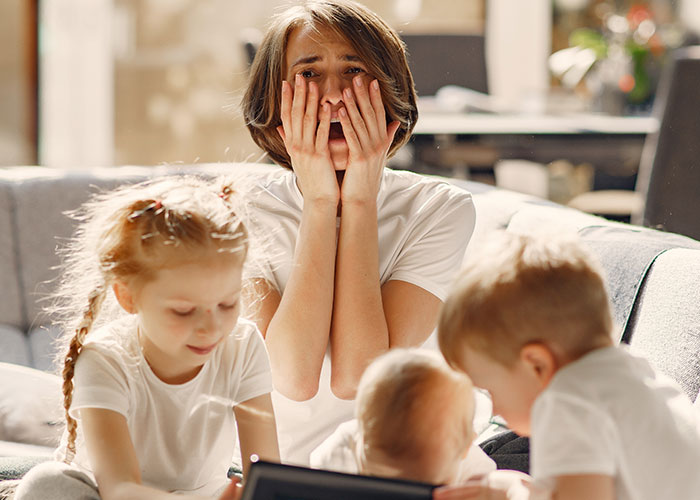 Stressed woman sitting on sofa with kids around her, illustrating family emergency and kicking out sisters kids situation.