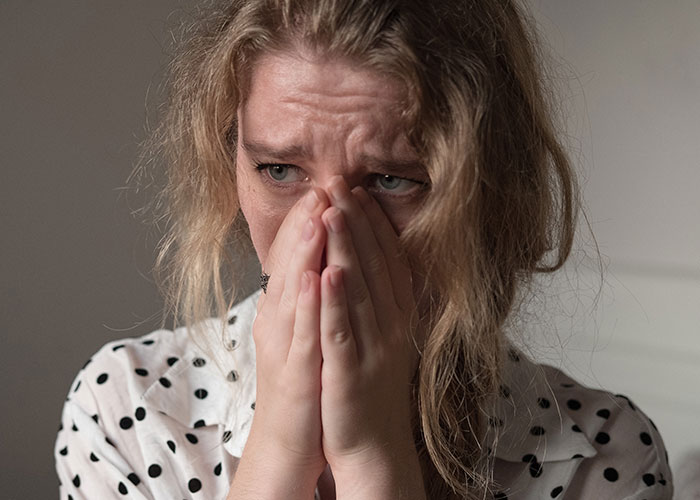 Woman in polka dot shirt covering face with hands, showing distress during a family emergency involving kicking out sister's kids.