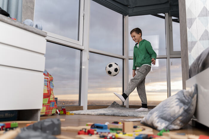 Young boy kicking a soccer ball indoors in a messy room, illustrating challenges of living next to horrible people.