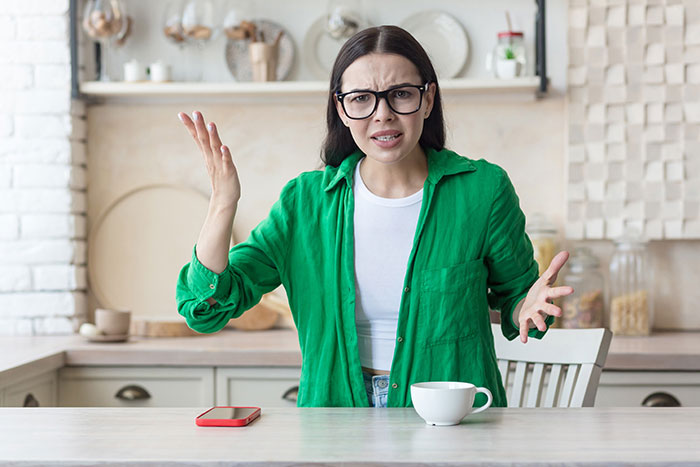 Young woman in green shirt expressing frustration while sitting at kitchen table, related to inheritance dispute and family traditions.