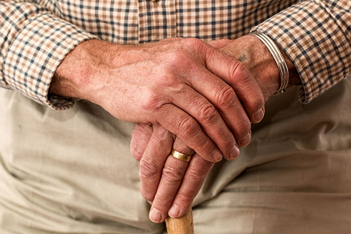 Elderly man wearing a gold ring and plaid shirt holding a wooden cane, symbolizing inheritance and family traditions.