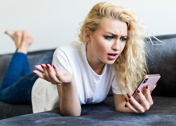 Young woman with blonde curly hair lying on a couch, looking frustrated at her phone, symbolizing stepkid relationship issues.