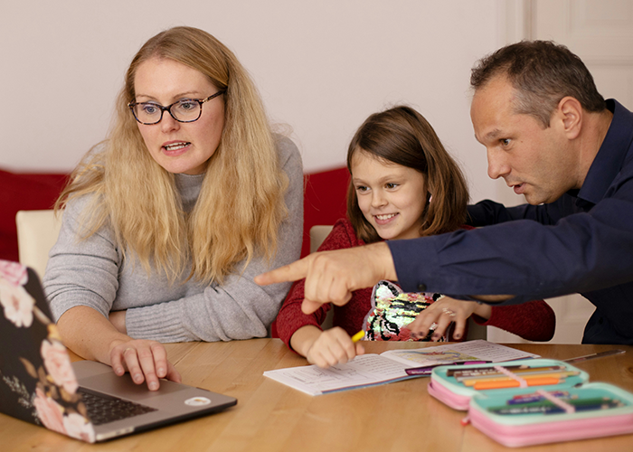 Woman with future stepkid and partner at table, using laptop and doing homework together in a home setting.