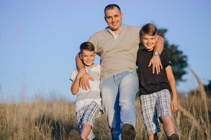 Man with two boys outdoors, representing a rich father taking son on fancy trips in a family setting.