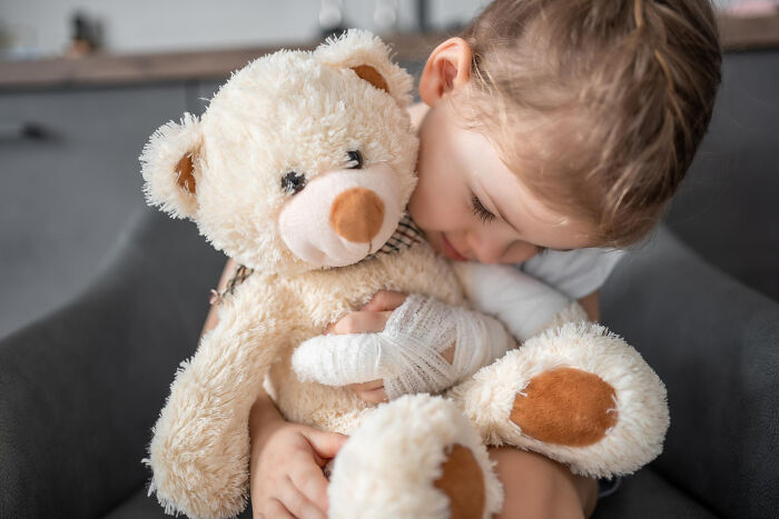 Young child with bandaged hands hugging a teddy bear, illustrating random things people did as kids not exactly normal.
