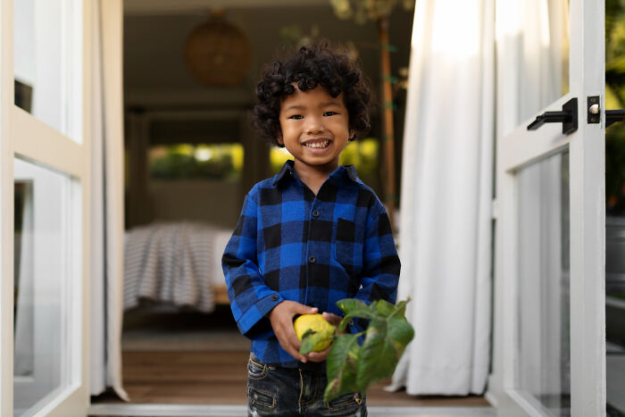 Smiling child in a blue plaid shirt holding a plant, illustrating random things people did as kids now seen as unusual.