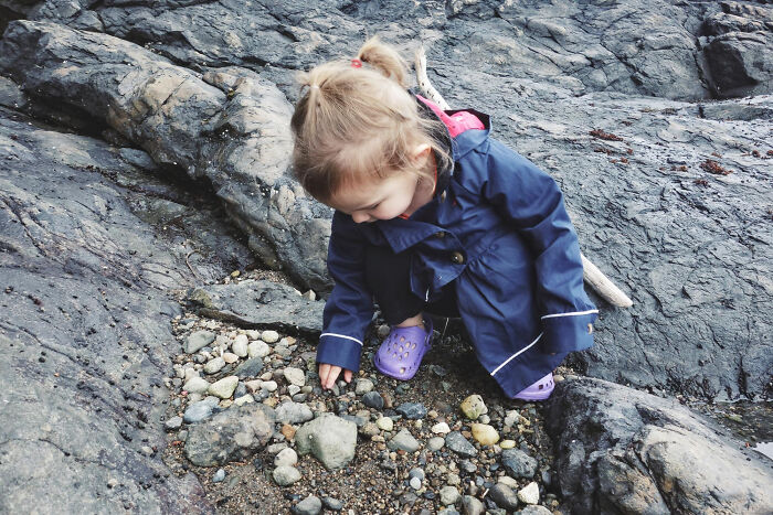 Young child exploring rocks and pebbles on a beach, reflecting on random things people did as kids not exactly normal.