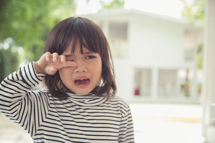 Young child crying outdoors wearing striped shirt, illustrating random things people did as kids not exactly normal behavior.