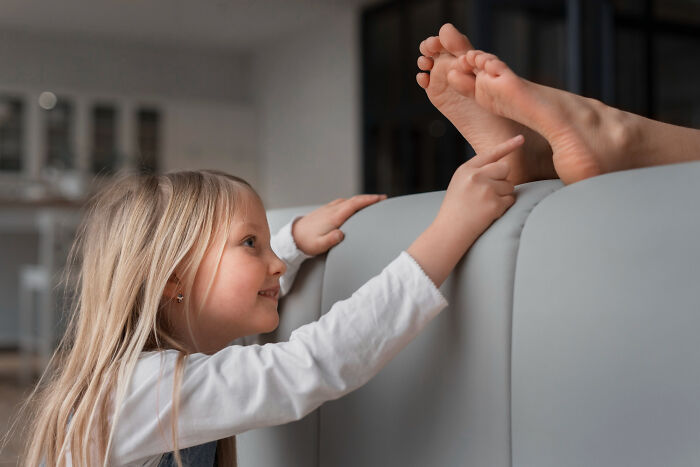 Young girl touching feet playfully on couch, representing random things people did as kids that weren’t exactly normal.